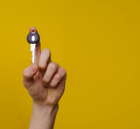 Mans hand with key isolated on yellow background with copy space. High quality photo.の写真素材