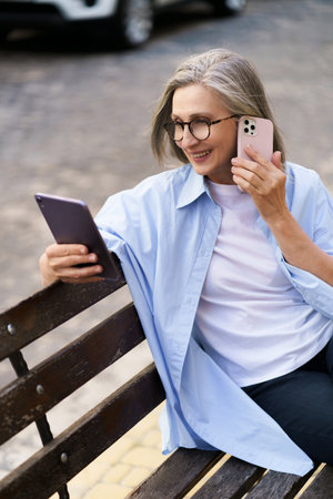 Happy senior woman is multitasking with a tablet PC and phone call on a busy city street. She showcases modern technology and active lifestyle in the elderly population. High quality photoの写真素材