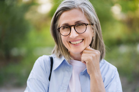 Happy mature woman with silver hair and glasses smiling outdoors, showcasing the beauty of aging and positive attitude towards life in the golden years. High quality photoの写真素材
