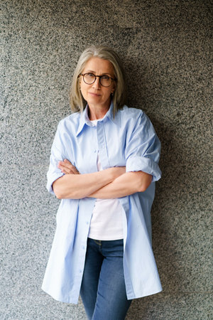 Confident and stylish senior woman with a seductive look standing near a wall in an urban environment, exuding independence and sophistication. High quality photoの写真素材