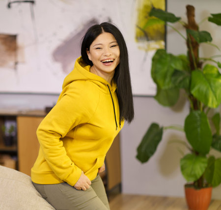 Happy Asian woman is leaning on the sofa and smiling at home. The image represents the concept of a happy and healthy lifestyle with a focus on biohacking. High quality photoの写真素材