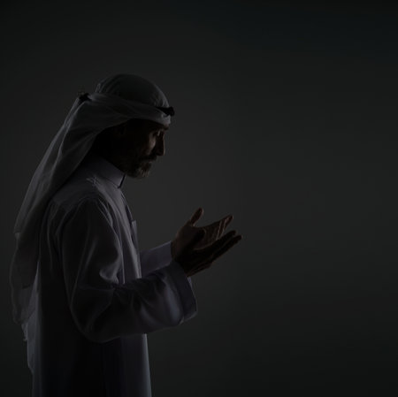 Muslim Arab man is prayer, raising hands to face with peaceful, serene expression. Copy space and portrays the mans devotion and spirituality in traditional Islamic context. Black and white portrait. High quality photoの写真素材