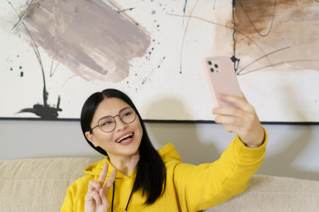 Asian student takes selfie with smartphone, utilizing the latest in mobile photography and communication technology. With glasses on, she captures self-portrait to share on social media or with friends online. High quality photoの写真素材