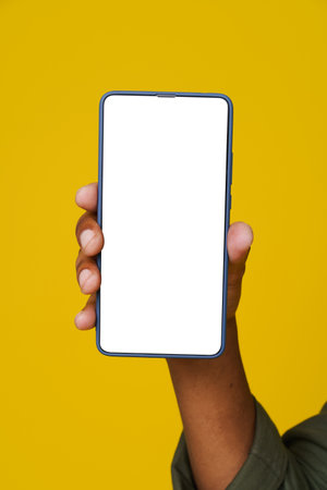 African mans hand holding phone with white blank screen on yellow background. Close up. Advertising concept. High quality photoの写真素材