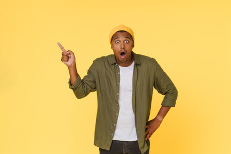 Amazed African man points to the side to copy space on yellow background. Advertising concept. High quality photoの写真素材