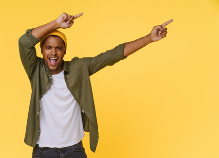 Excited African man points two hands to the side to copy space on yellow background. Product placing, advertising concept. High quality photoの写真素材