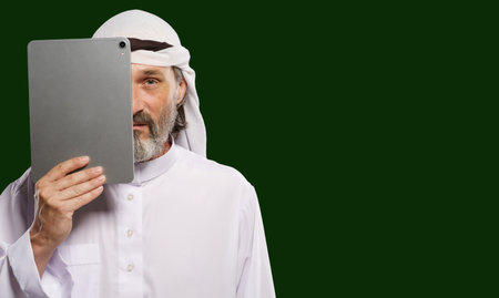 Islamic censorship online. Muslim Arab person holding tablet PC covering half of face symbolize concept of issues of privacy, security, and anonymity in digital world with modern and contemporary lifestyle perspective. High quality photoの写真素材