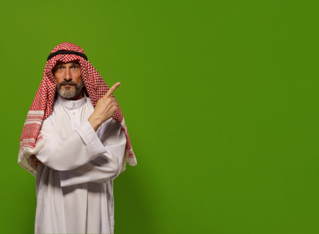 mature Muslim man in traditional dishdasha points his finger towards copy space symbolizing concept of Sharia law, Islamic legal system based on teachings of Quran and Hadith. authority, leadership, and principles of justice and ethics within the legal framework of Sharia law, with copy space for additional text or design elements. High quality photoの写真素材