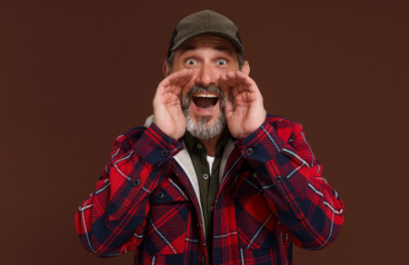 Country style concept. American country man or farmer made megaphone with hands going shout isolated on brown background. High quality photoの写真素材