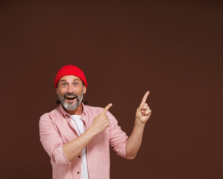 Amazing reaction. a mature European caucasian man points with both hands to the side with copy space isolated on brown. Product placement concept. High quality photoの写真素材