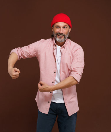 Mature handsome concept. Show strength. middle-aged European man with gray beard showcases his physical strength by flexing his biceps and clenching his fists, exuding confidence and determination. High quality photoの写真素材