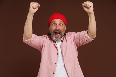 Sports fan victory concept. Happy mature handsome European caucasian man holds clenched fists above his head celebrating win of his team command. High quality photoの写真素材