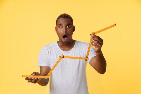 Concept of income growth, amazed African American man holding folding ruler and showing growth chart on the stock exchange. Man is standing on bright yellow background with copy space for designers to add their own text or graphics. High quality photoの写真素材