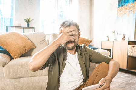 Cheater online. Man covering face with facepalm, holding mobile phone. Hacker concept. He may have been caught doing something wrong or possibly caught in act of hacking or online fraud. High quality photoの写真素材