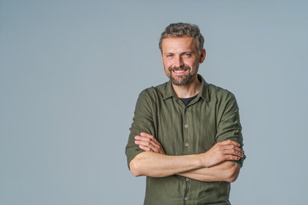 Cheerful and confident man in casual wear stands on white background with hands in pockets, smiling and radiating positive energy. Can be used to represent happiness, positivity, confidence, and friendliness. High quality photoの写真素材
