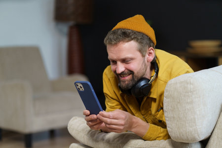 Man in casual spending his leisure time home on sofa, engrossed in phone. He texting someone using...