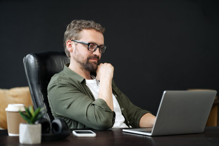 Wise, caucasian man captured in portrait, sitting at desk in home office. He appearing thoughtful, as he works on computer. Sense of professionalism and productivity in a home work environment. High quality photoの写真素材