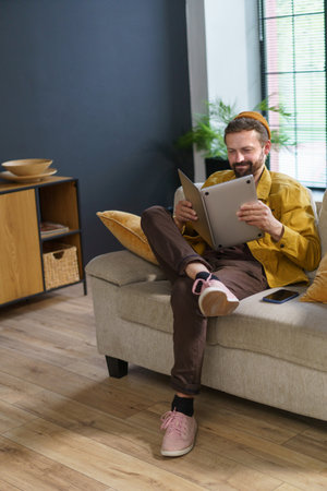 man sitting with laptop in incorrect position, showcasing ineptitude as worker. Mans lack of proper work habits and efficiency reads laptop like book, displaying misguided approach to using device. High quality photoの写真素材