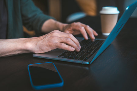 Close-up of mans hands typing text message on laptop keyboard. Work-from-home setup and modern communication technology. The man focused on task, with laptop screen out of focus in the background. High quality photoの写真素材