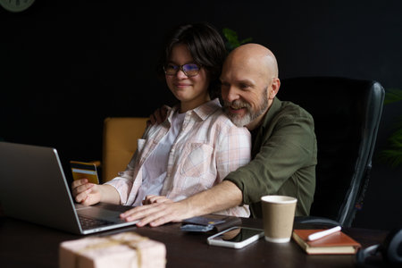 Joyous bond between happy father and teenager daughter. Online shopping experience, engaging in shared activity. Father holding credit card in hands, ready to enter payment data for purchase. . High quality photoの写真素材
