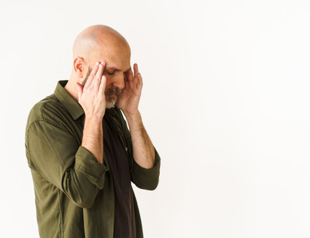Mature man experiencing headache holds head with both hands. Concept of headache, conveying pain and discomfort that can accompany such experience. . High quality photoの写真素材