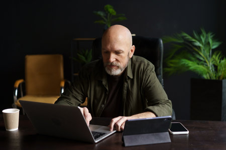 Man diligently working on his laptop from the comfort of his home. With a dedicated workspace and a focused expression, he embraces the concept of online work and remote productivity. . High quality photoの写真素材