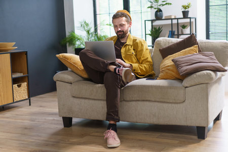Man sitting at home, engrossed in laptop, types comments in social networks on internet. Man with a unique and eccentric demeanor, giving him appearance of weirdo or crank. . High quality photoの写真素材
