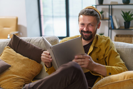 Student engaging in deceptive behavior sit on sofa and hold laptop like book indoors. Concept of cheating, highlighting students questionable actions in academic context. High quality photoの写真素材