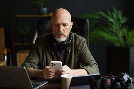 Modern lifestyle of individuals who work remotely or from comfort of own homes. Mature man multitasking at home. He texting message on phone while also working on computer. . High quality photoの写真素材