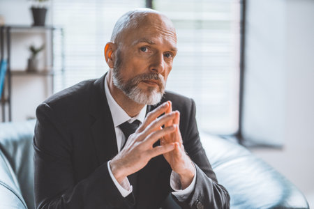 Wise senior businessman seated in office, deep in thought, gazes directly into camera. Seasoned professional with profound understanding of business world. Senior businessmans thoughtful expression. High quality photoの写真素材