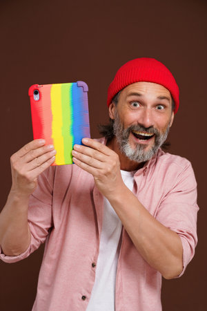 Coming out LGBTQ concept. Happy European man smiling while holding tablet PC in colorful rainbow case. Modern man with digital device represents LGBTQ community. High quality photoの写真素材
