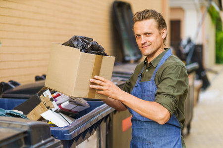 Man sorting garbage before throwing it into trash can. Man, possibly service worker, is engaged in preparation of waste for further utilization.Importance of recycling and sustainability in waste management. . High quality photoの写真素材