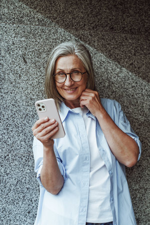 Concept of communication in old age, mature senior woman using mobile phone for texting and internet messengers. Womans active engagement with technology and desire to stay connected in digital age. High quality photoの写真素材