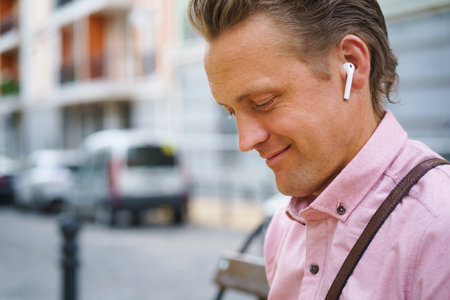 Moment of pure happiness as man with closed eyes enjoys listening to music on bench in bustling urban city. He fully immersed in music, finding relaxation and contentment in melodies. . High quality photoの写真素材