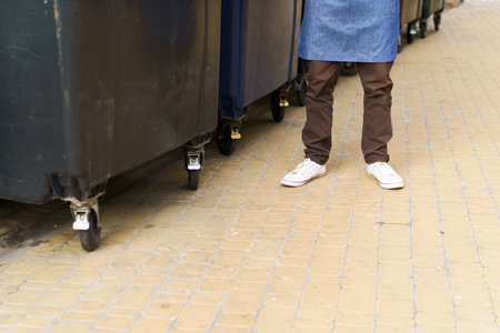 Garbage city trash cans, featuring view of trash cans in back yard and feet of kitchen worker. Presence of trash cans highlights importance of proper waste management and recycling in urban areas. . High quality photoの写真素材