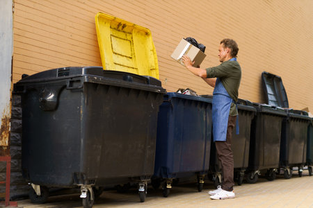 Diligent kitchen worker or waiter is seen responsibly disposing of garbage in city trash can. With sense of responsibility and cleanliness, he ensures proper waste management in urban environment. . High quality photoの写真素材
