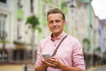 Mid aged man engaged in texting a message while being outdoors. With his mobile phone in hand, he utilizes digital communication to connect with others in the urban environment. High quality photoの写真素材