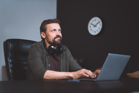 Worker daydreaming while sitting in office. Man dressed in casual wear, typing on laptop. However, distant gaze and relaxed posture suggest that he lost in thoughts, indulging in moment of dreaming. High quality photoの写真素材