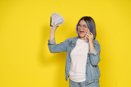 Happy Teenager Takes Phone Call While Holding Wallet With Cash Money, Ready For Shopping And Other Things That Children Love To Buy. Isolated Against Yellow Background, Financial Independence For Teenager. High quality photoの写真素材