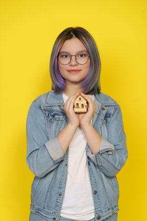 Girl Teenager Holds Little House, Symbolizing Concept Of Care About Household And Creating Positive And Cheerful Atmosphere For Children Home. Isolated Against Vibrant Yellow Background. High quality photoの写真素材