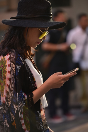 Woman standing on street styled with hat and glasses playing mobile phoneのeditorial素材