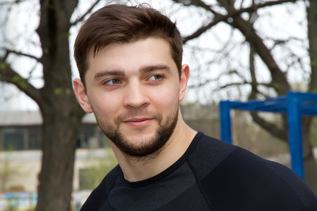 portrait of young attractive man athlete smiling at the stadium, standing in a black tracksuitの写真素材