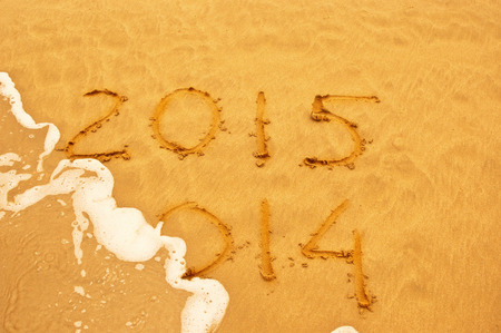 New Year 2015 is coming concept - inscription 2014 and 2015 on a beach sand, the wave is starting to cover the digits 2014 の写真素材