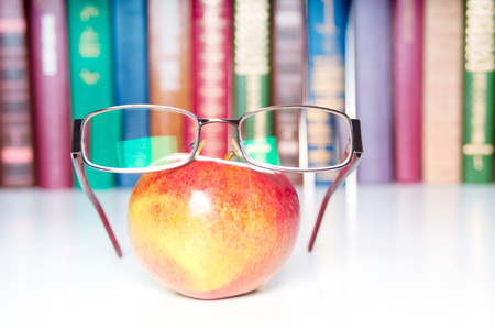 An apple with eyeglasses and colorful books on backgroundの写真素材
