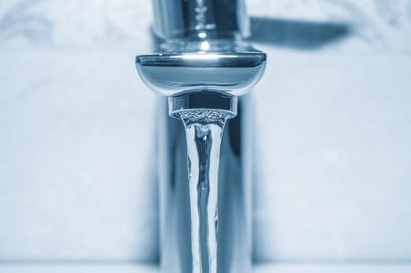 Faucet with flowing water close up on blue backgroundの写真素材