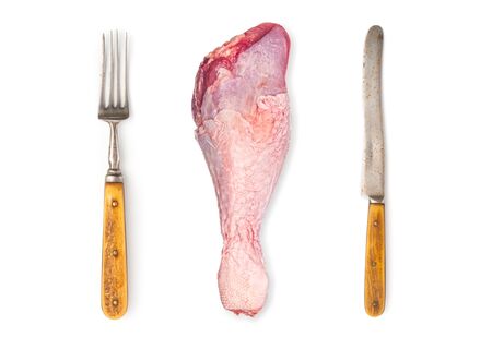 Raw turkey drumstick with vintage knife and fork on white background
