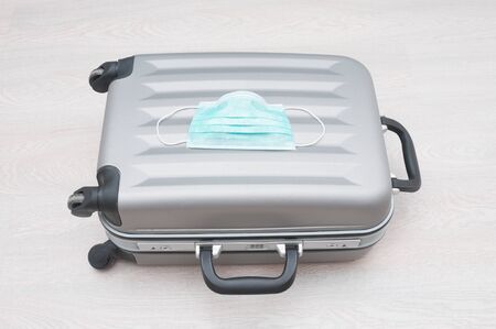 Gray travel bag and virus protection mask  on wooden background