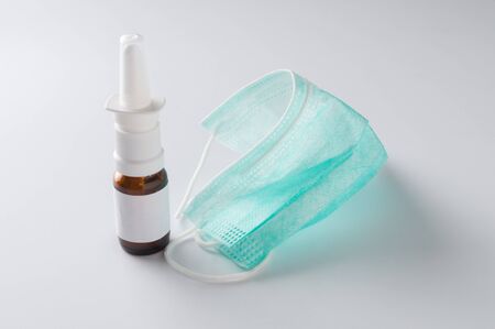 Nasal spray and medical virus protection mask on gray background