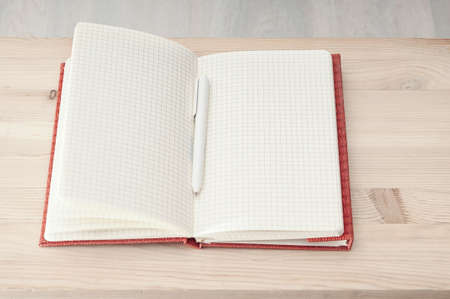 Open notepad with pen on wooden background