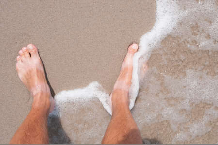 Tanned bare men's feet on a sea coastの写真素材